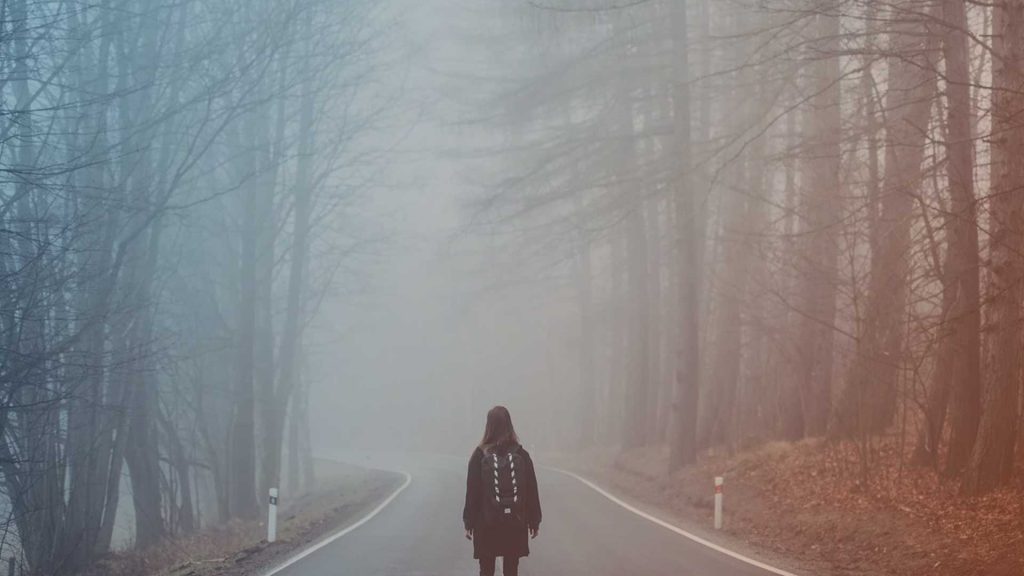 Frau steht an einsamem Waldweg - Symbolbild für Angst