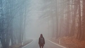Frau steht an einsamem Waldweg - Symbolbild für Angst