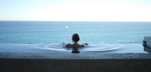 Frau entspannt beim Bad im Pool mit Blick auf Meer.