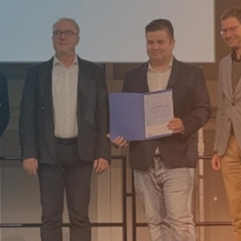 Vier männliche Personen stehen auf einer Bühne und empfangen einen Preis.