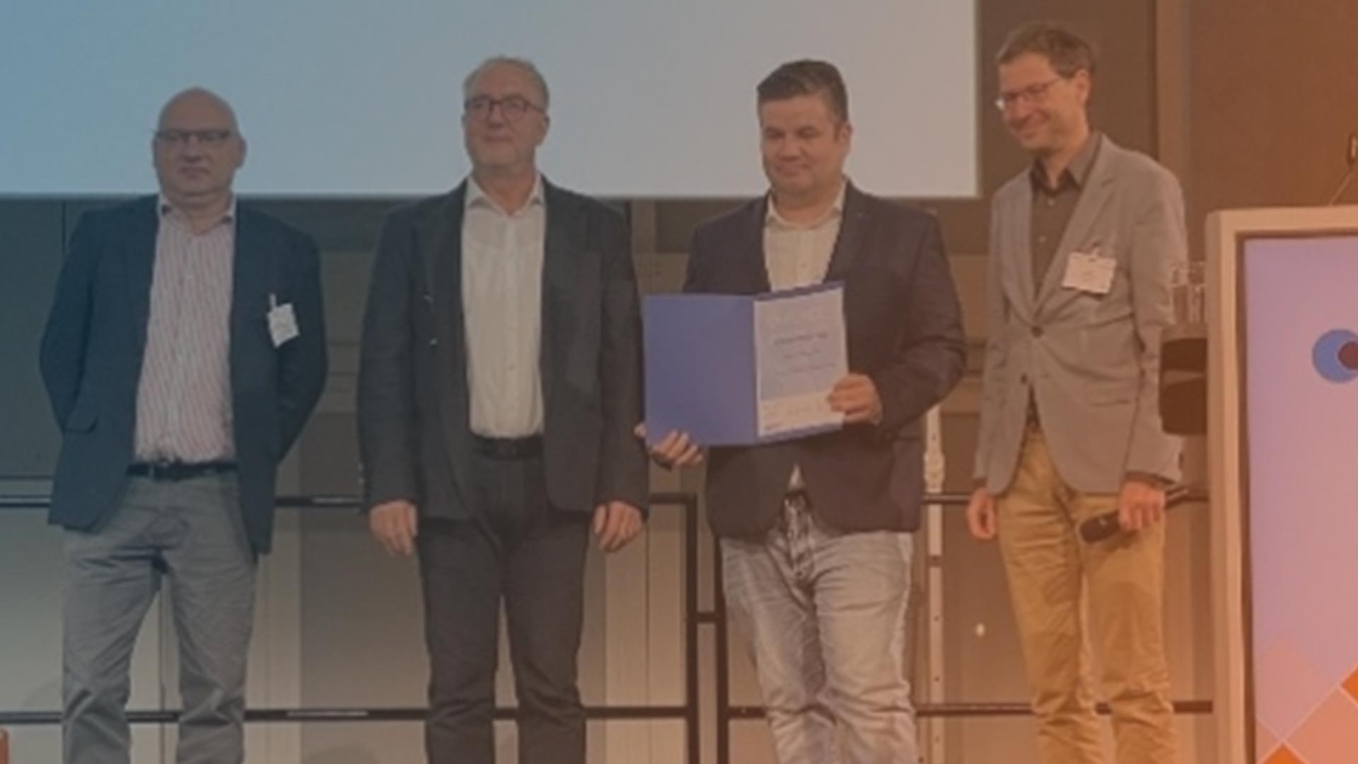 Vier männliche Personen stehen auf einer Bühne und empfangen einen Preis.